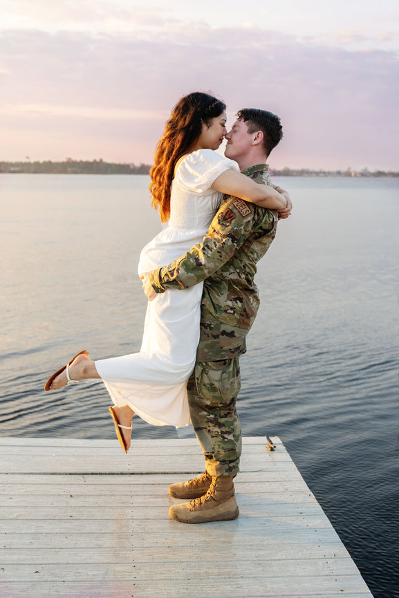 Military couple joyfully hugging on a lakeside dock