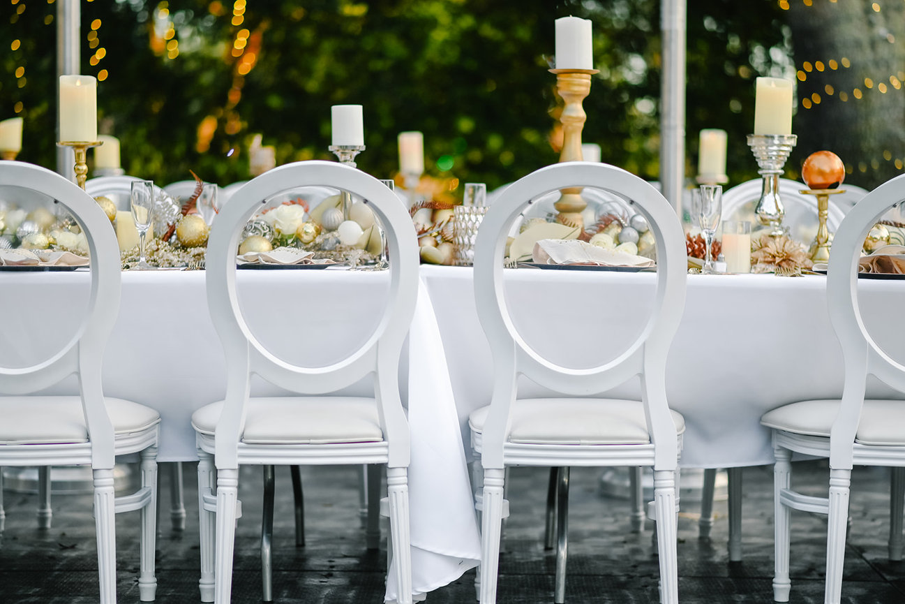 Elegant outdoor dining setup with a long table, white chairs, candles, and festive decor.