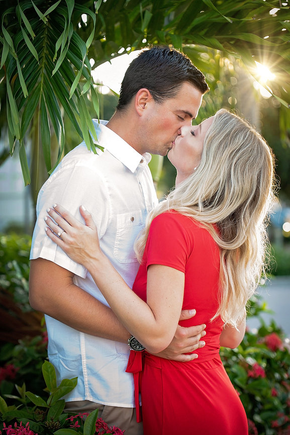 Romantic couple kissing amid lush greenery and floral backdrop, capturing a warm, intimate moment.