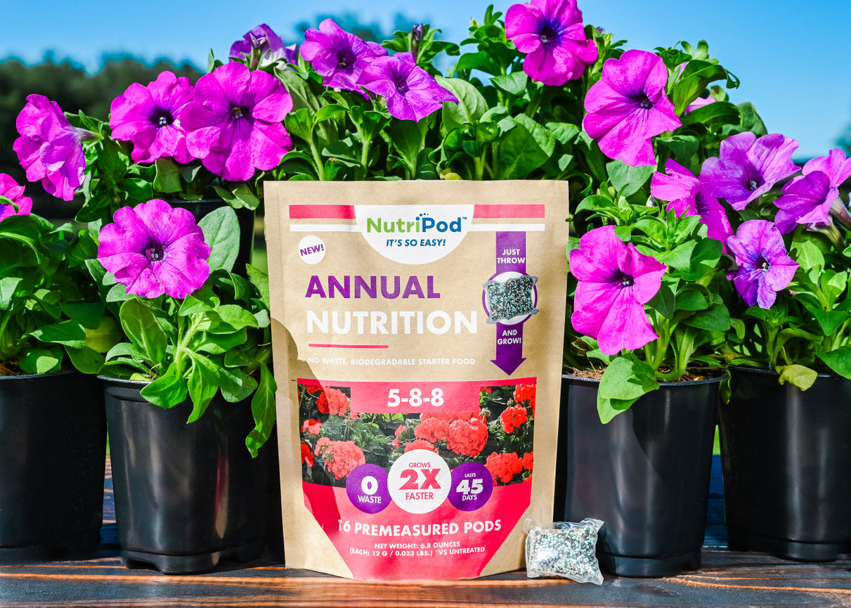 NutriPod Annual Nutrition bag with premeasured pods, surrounded by blooming purple flowers in pots.