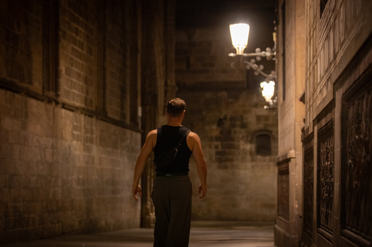 Person walking alone down a dimly lit historic alley with stone walls and ornate street lamps. Barcelona night