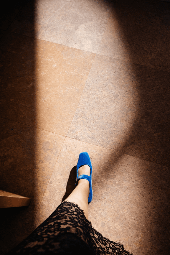 A person in blue shoes and a black lace skirt steps into light on a tiled floor.