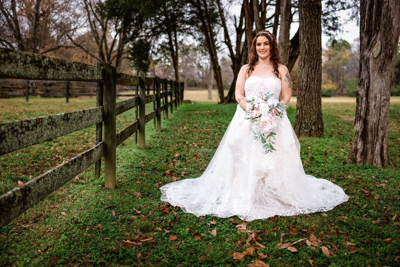 Bride posing outdoors in a lace wedding gown, surrounded by rustic wooden fences and autumn leaves during her Fairhope countryside wedding session.