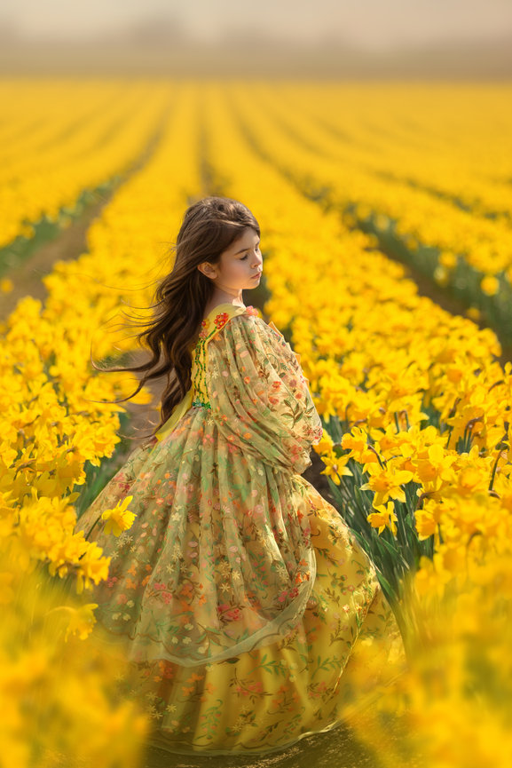 Girl in a colorful dress walking through a field of yellow flowers