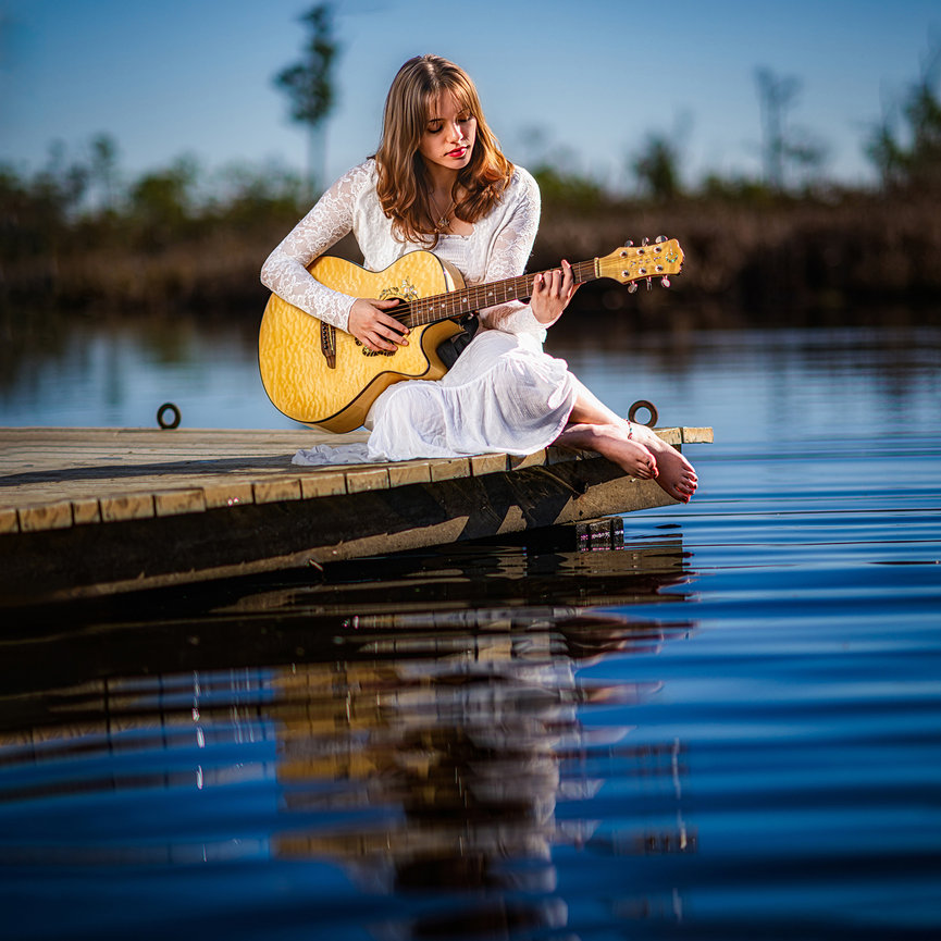 High school senior girl with acoustic guitar at golden hour over water — fine art waterfront senior portrait session by Swartz Portraits Katy Sugar Land Houston Texas