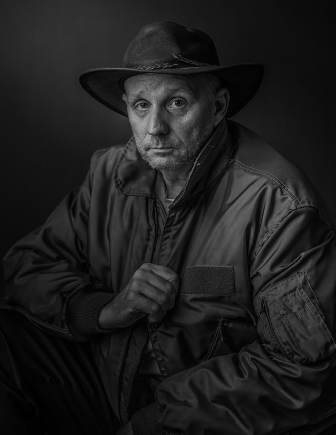 Author Ty Swartz in a wide-brim hat and dark jacket, a moody black-and-white cinematic portrait against a black background.