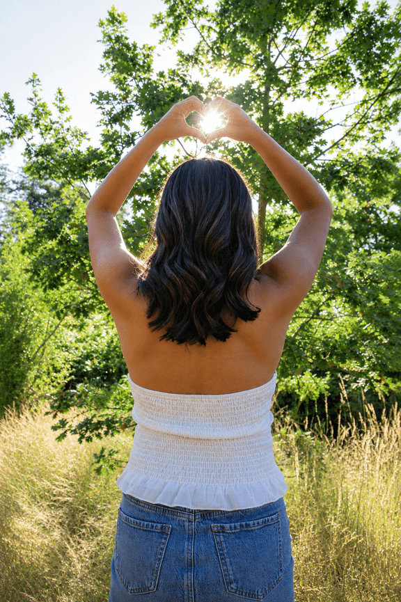 Woman seen from behind with arms raised in a sunny field.