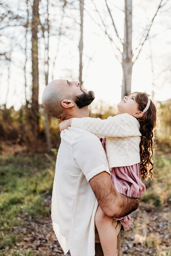 a father holds his young daughter as both look up into the sky in a Huntsville, Alabama family photoshoot