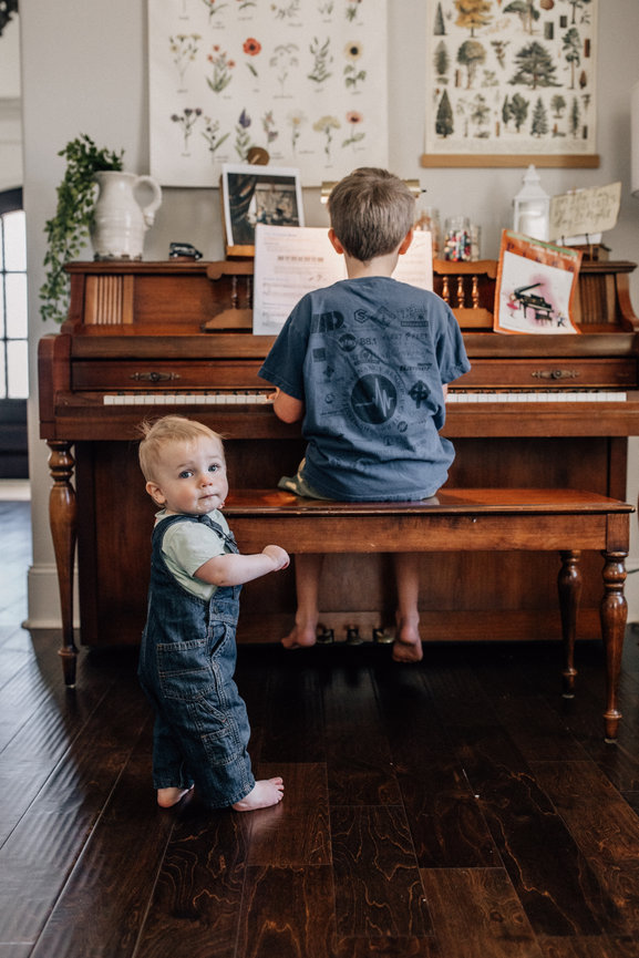 a baby boy looks back at the camera as his brother plays a piano in a Huntsville Alabama family photoshoot