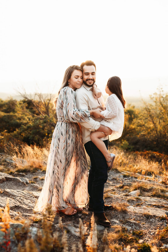 A mother hugging her husband and daughter at High Point State Park, New Jersey during their golden hour family photography session.