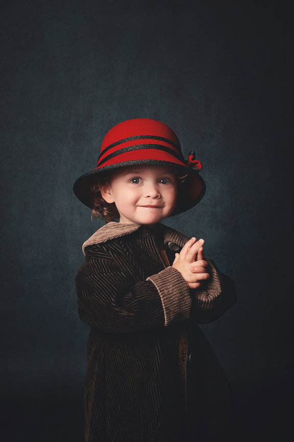 A smiling toddler in a red hat and green coat claps her hands