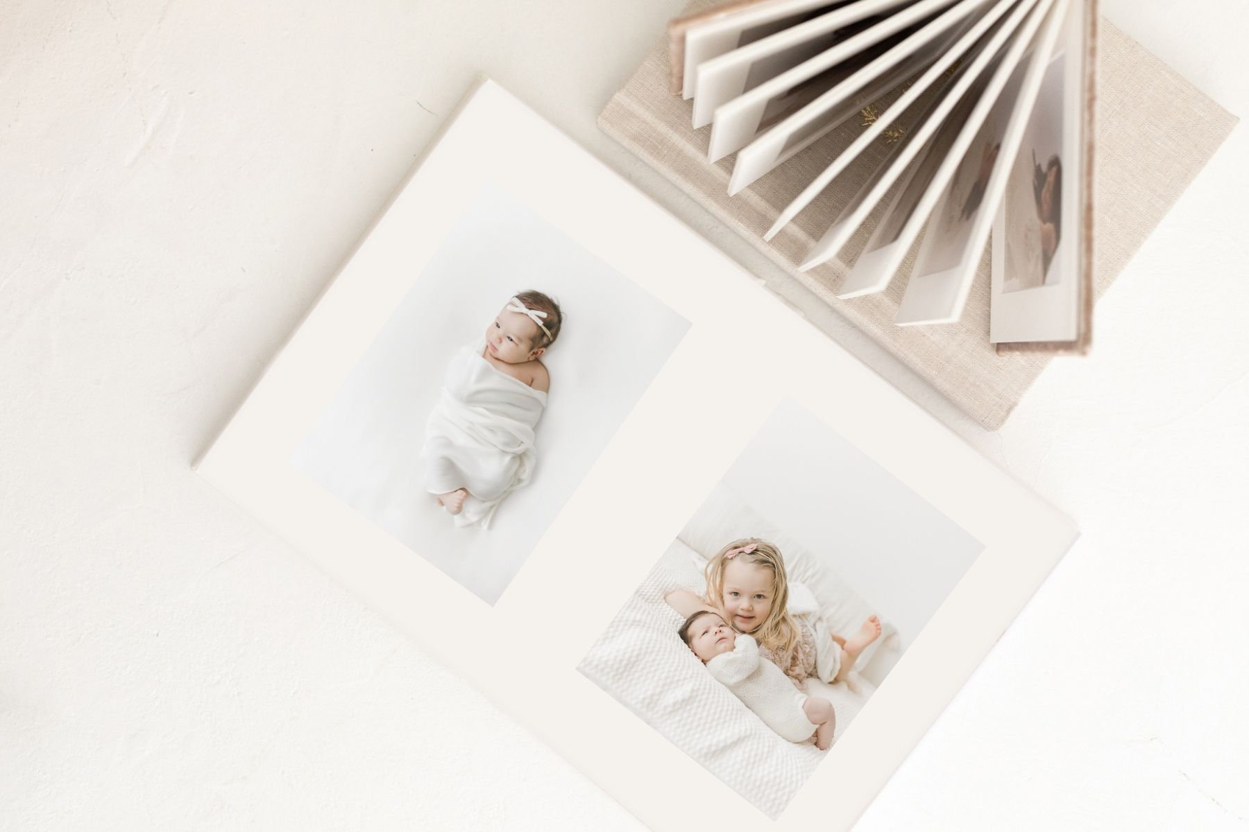Newborn baby photos displayed in a soft-bound photo album on a neutral background.