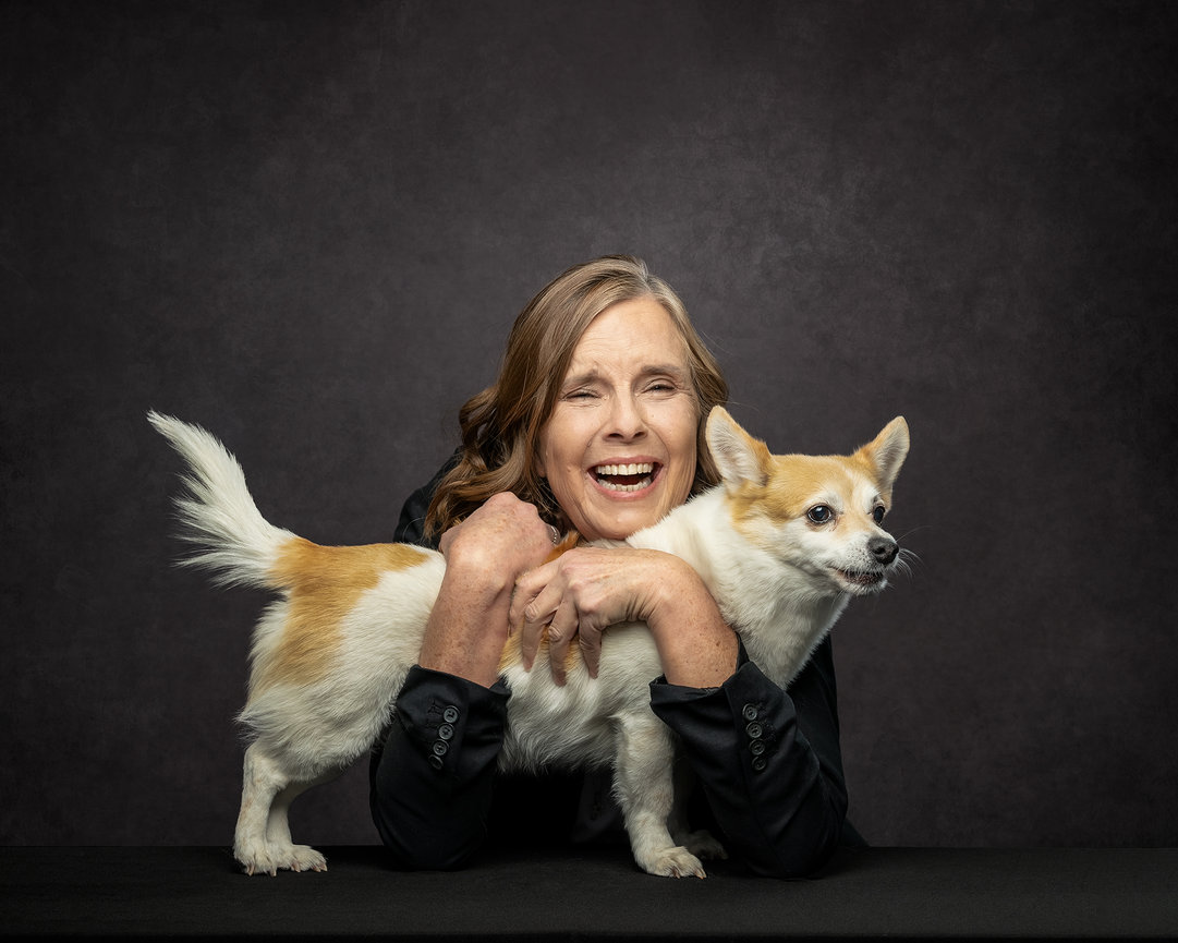Woman smiling with a small dog on a dark background.