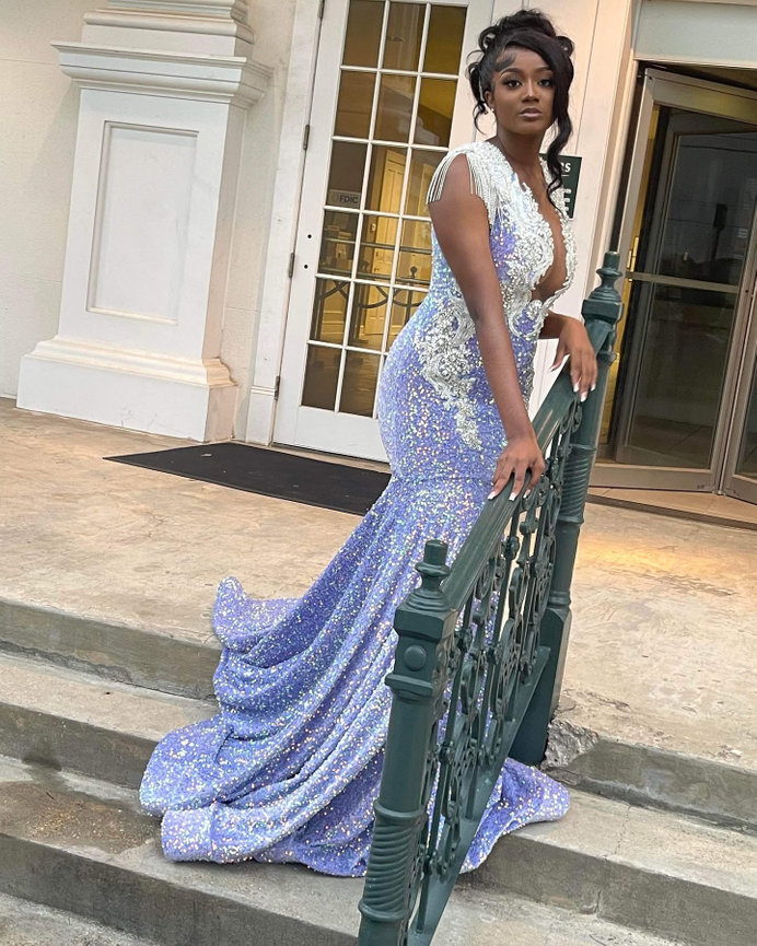 Woman in a sparkling blue gown with lace detail stands on steps near a railing and building entrance.