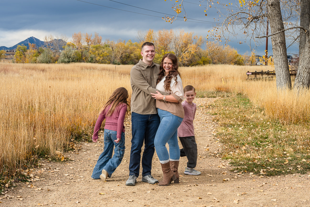 A young couple snuggle close together while their children run circles around them. Everyone is giggling.