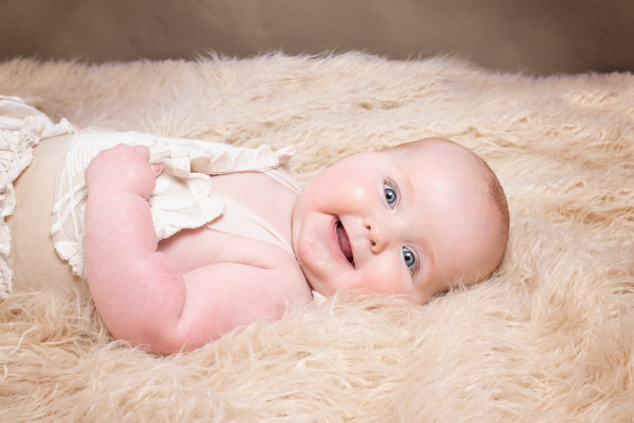 Smiling baby lying on soft, fluffy blanket.