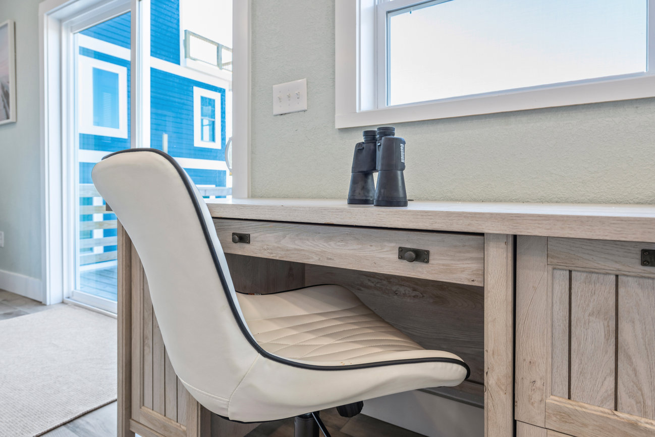 Modern home office with a white leather chair, wooden desk, and a pair of binoculars by the window.