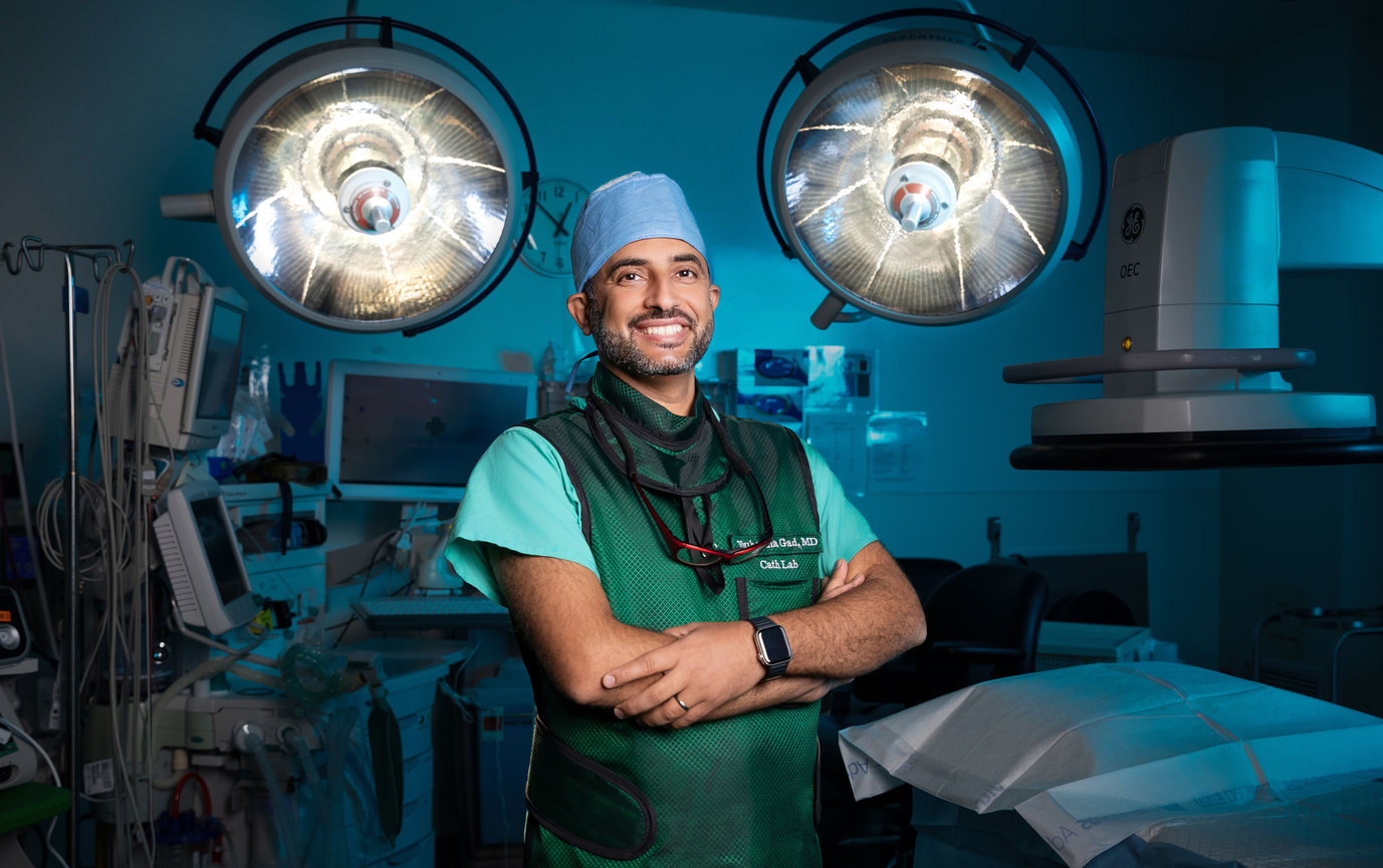 Surgeon standing in an operating room with surgical lights overhead.
