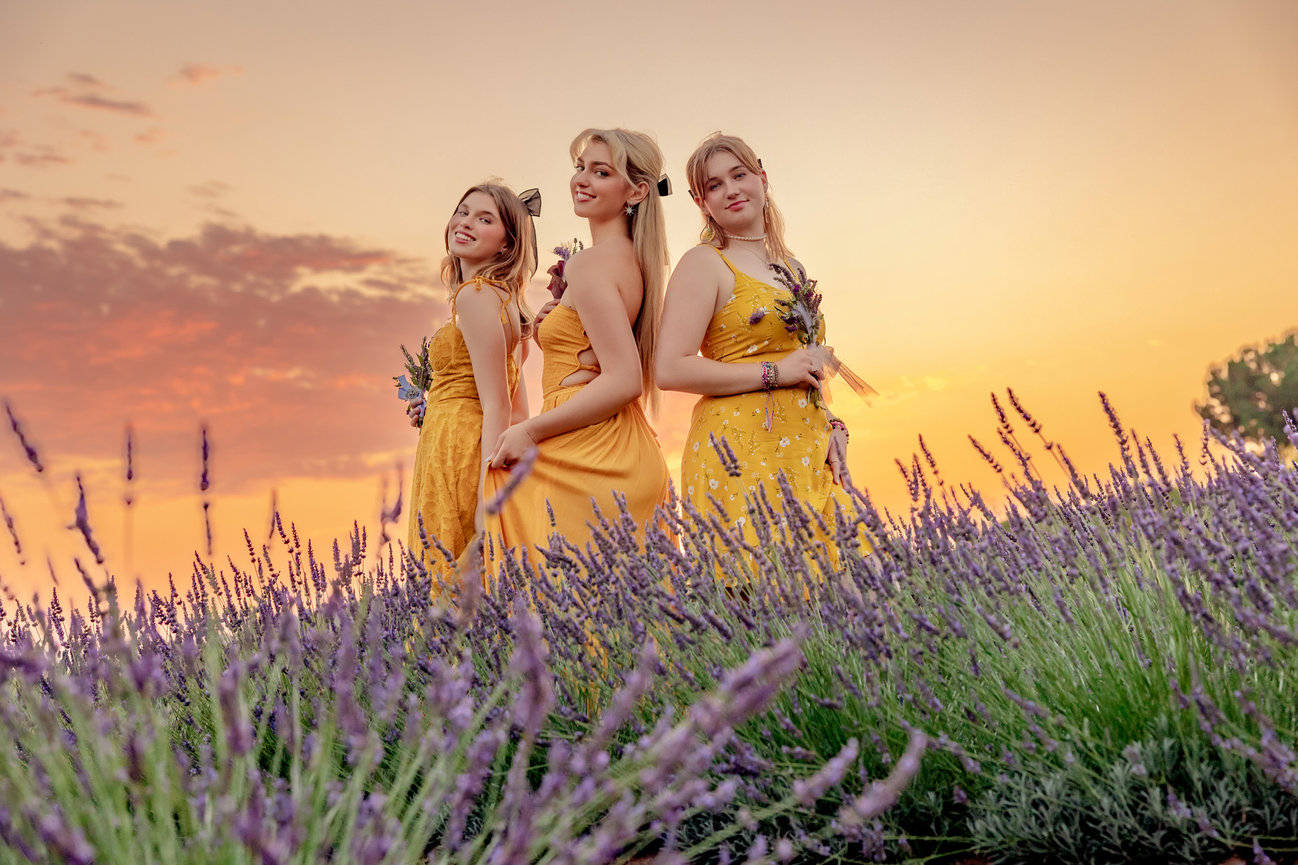 THREE HIGH SCHOOL SENIOR GIRLS STYLED IN YELLOW, STANDING IN A LAVENDER FIELD AT SUNSET .