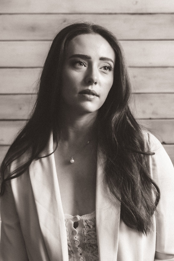 Woman with long hair in a blazer, standing against a wooden wall. Black and white photo.