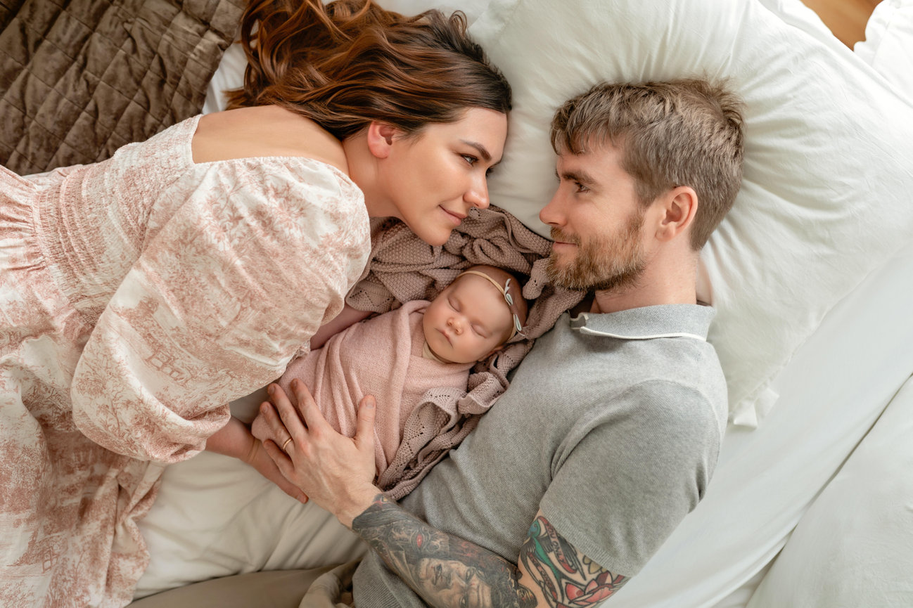 Parents gazing at their sleeping newborn in bed