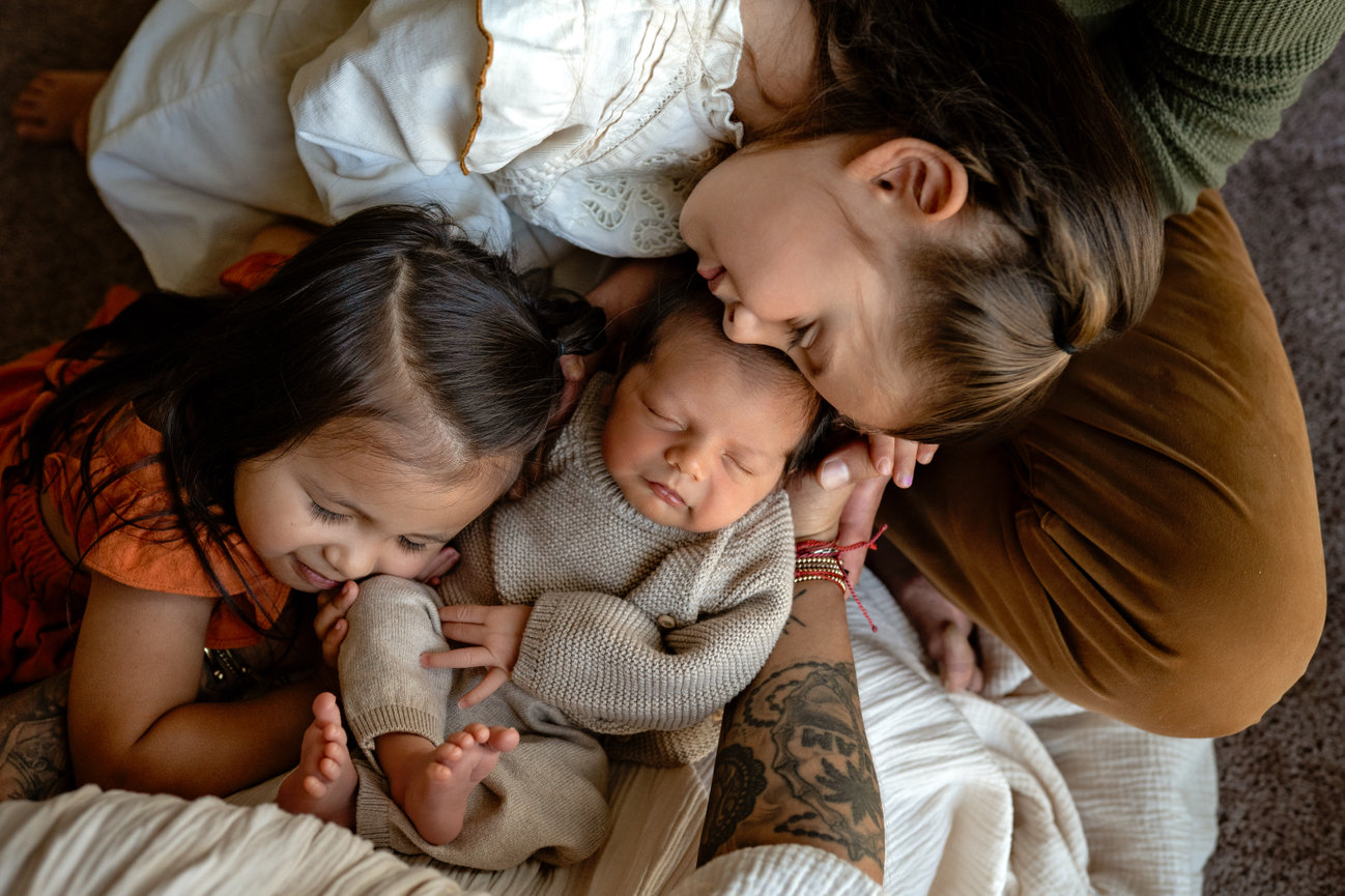Three children cuddling around a sleeping newborn on a bed- Melissa madden photography