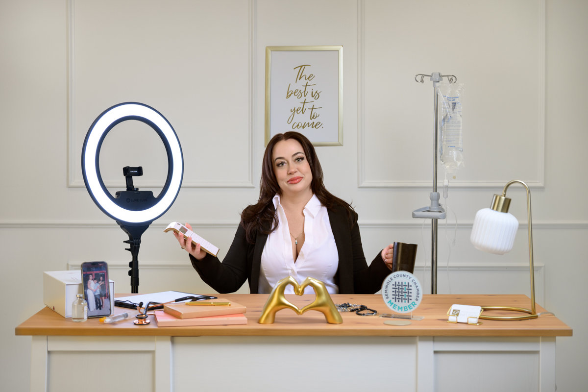Women's portrait photography Orlando - business owner at styled desk with ring light IV pole and Seminole County Chamber badge, She's More Than by Karen K Photo