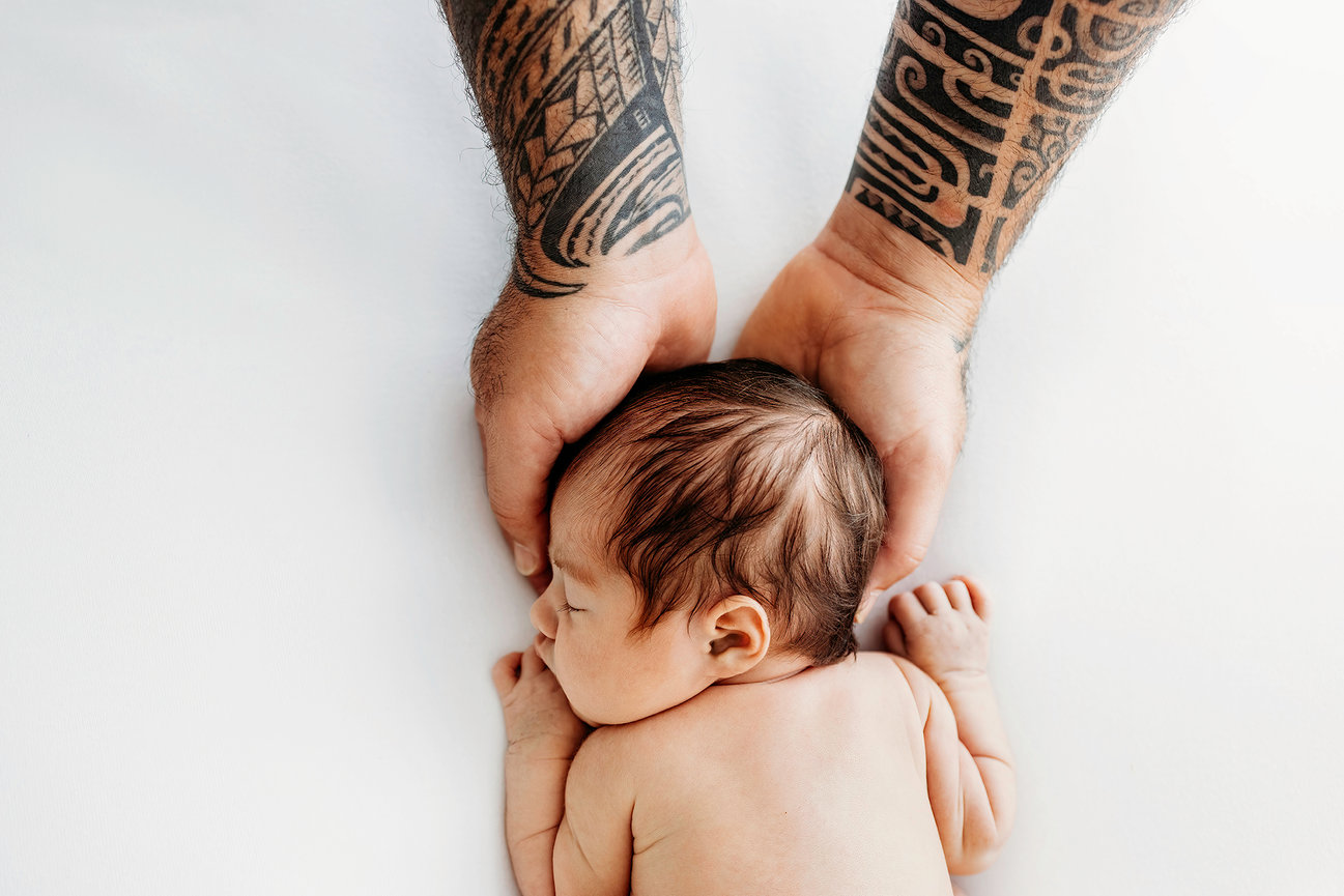 Tattooed arms cradling a sleeping newborn on a white background.