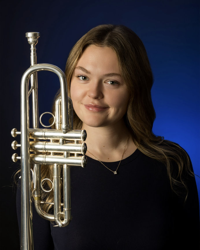 Smiling woman holding a trumpet against a blue studio backdrop.