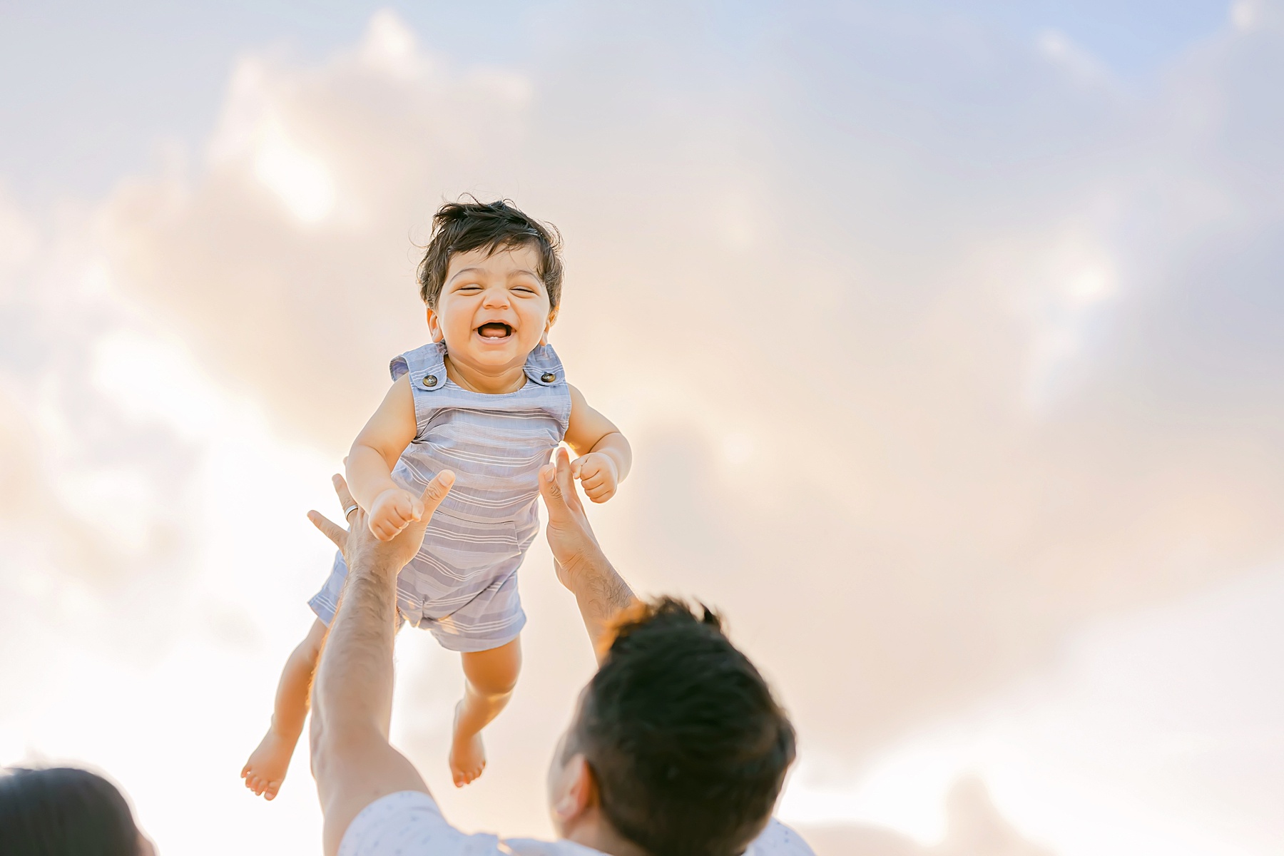 baby being thrown in air on beach by dad wearing blue overalls