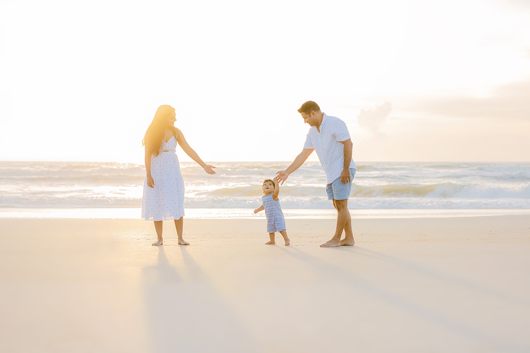 family of three walking at sunrise on the beach