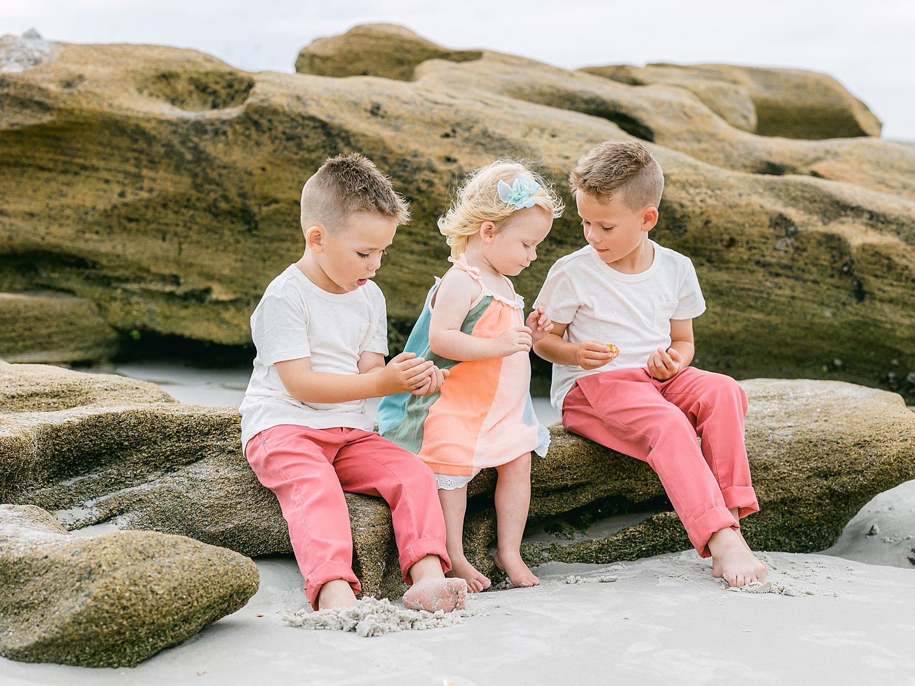 three children sitting on the rocks at the beach