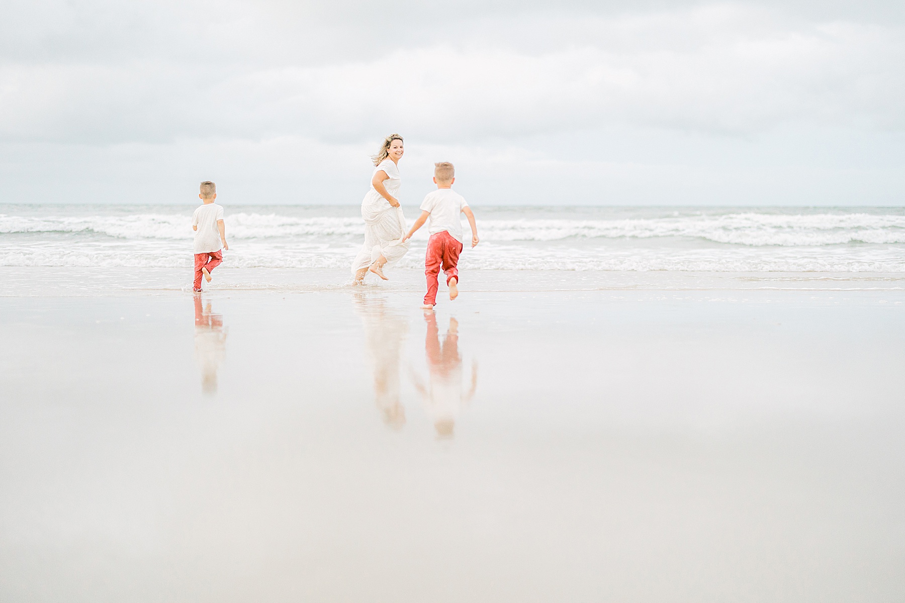 Woman running in white dress on the beach with two children