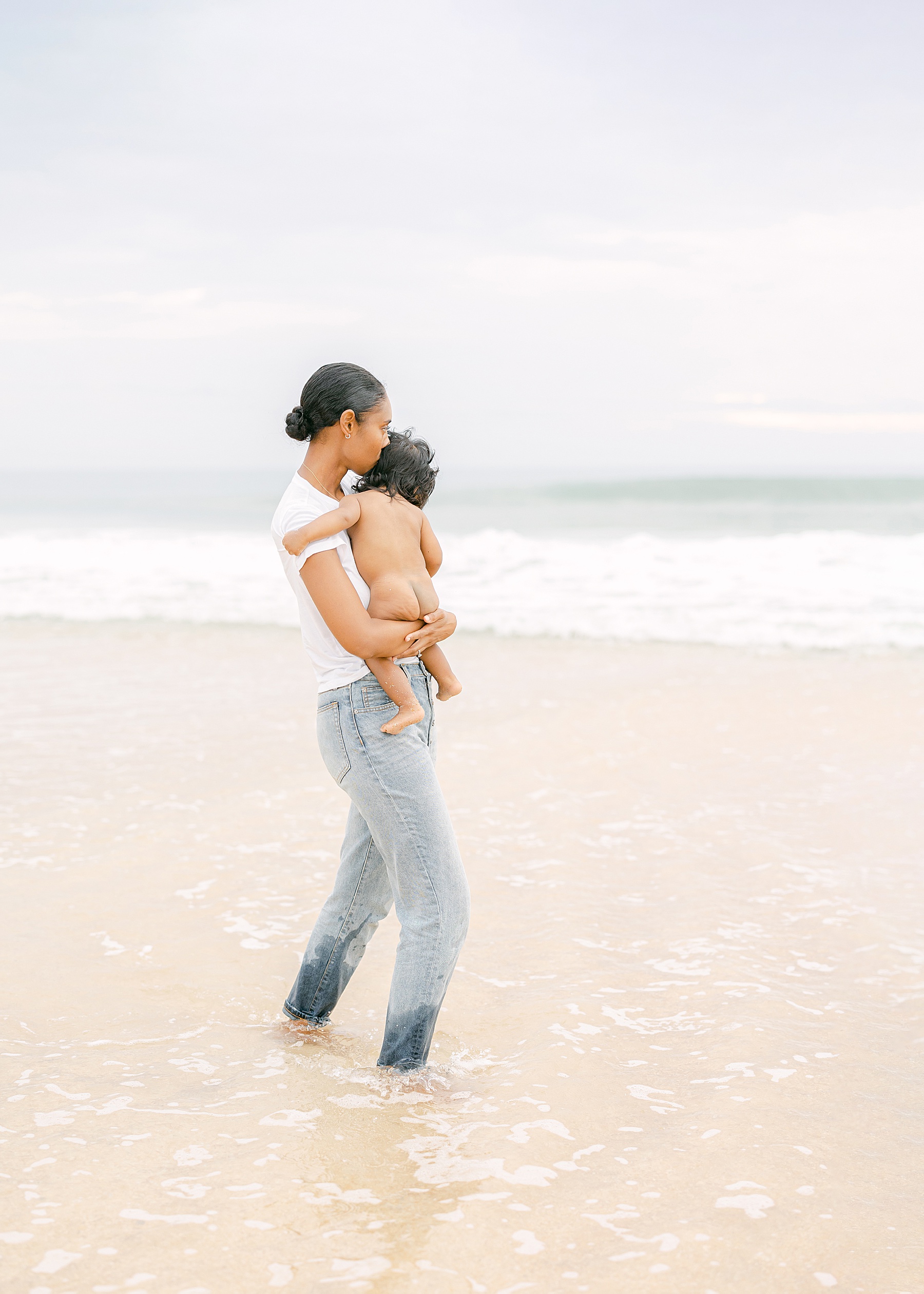 mom kissing baby by the water wearing jeans