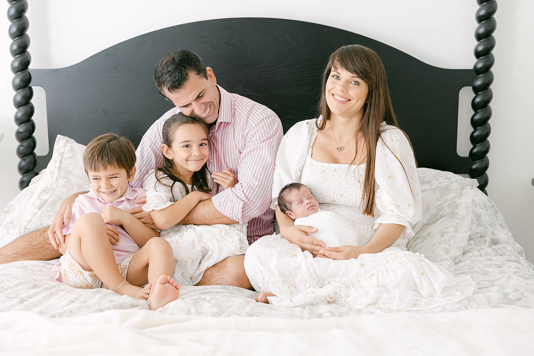 family sitting on be together white comforter holding newborn babty