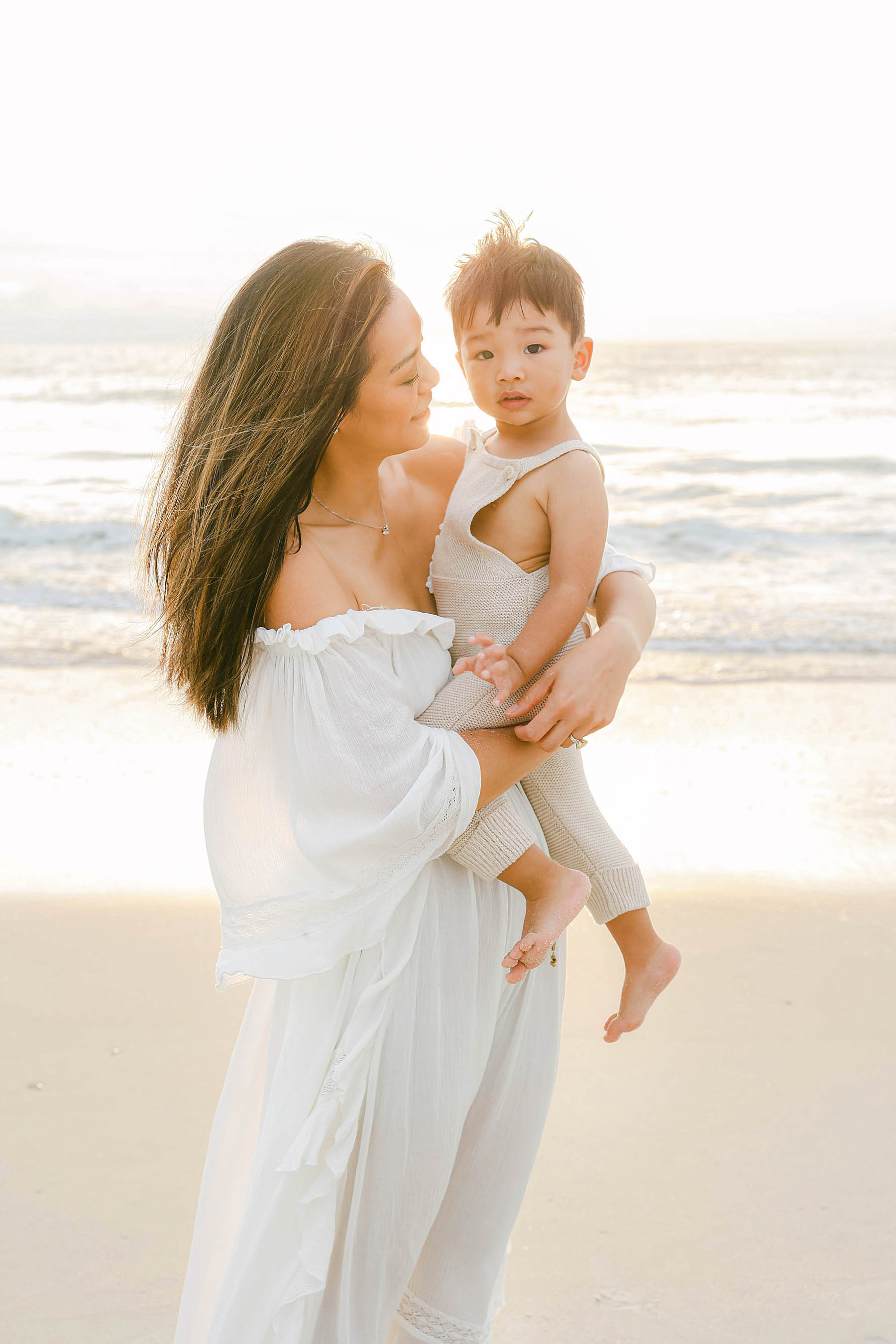mom holding baby boy wearing tan onsie on the beach