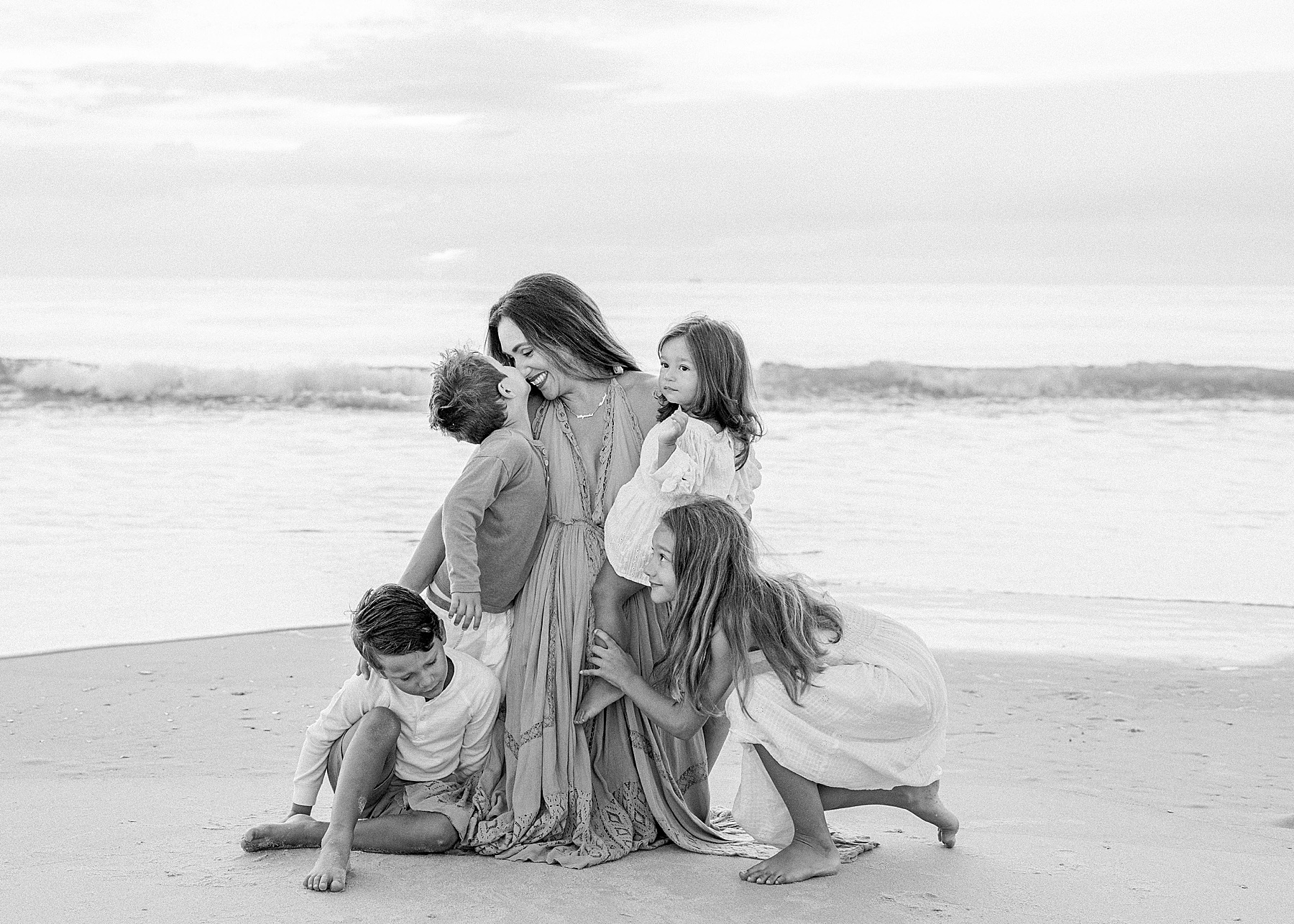 woman kneeling on beach in long dress with children