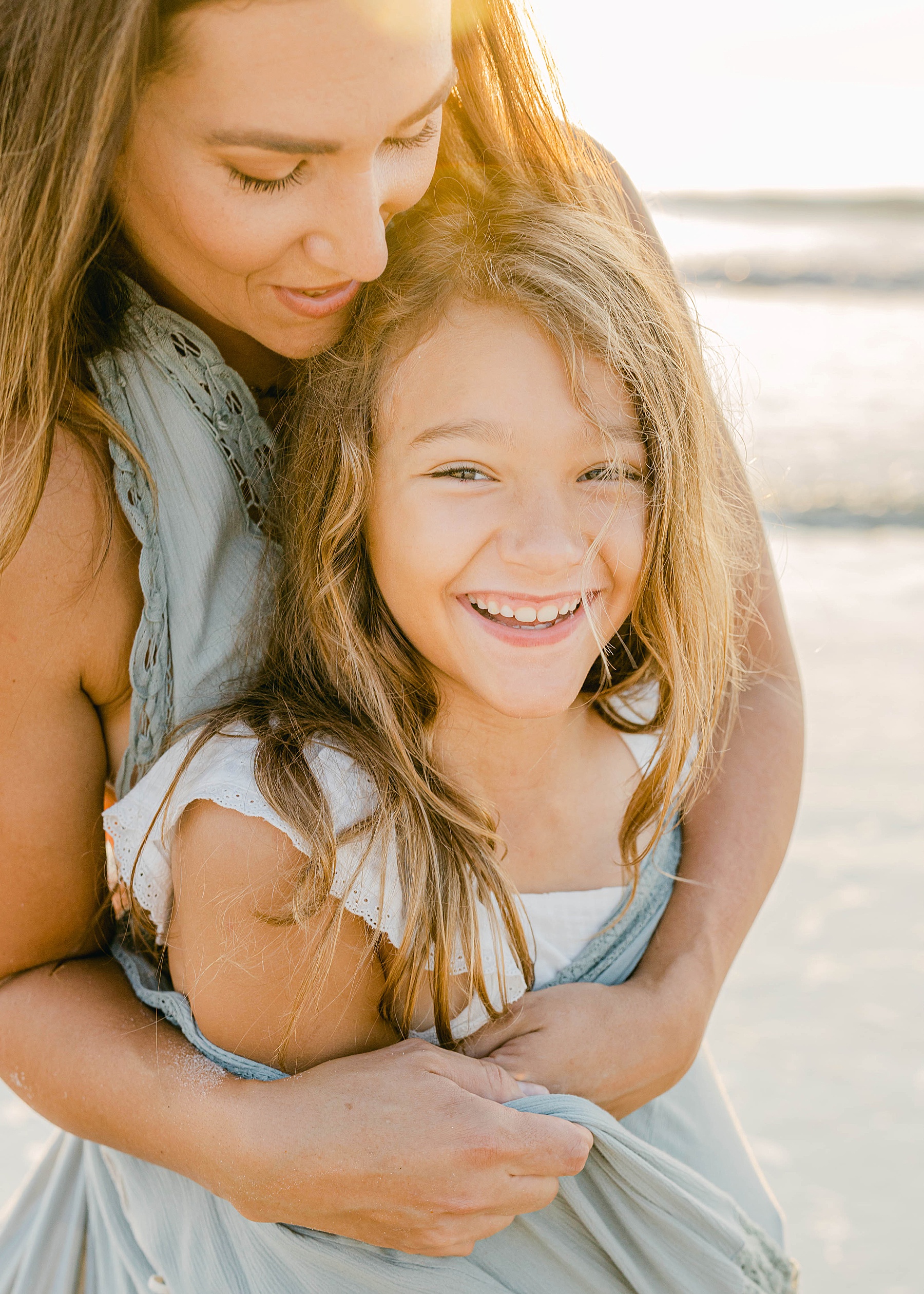 woman holding daughter laughing on the beach at sunrise