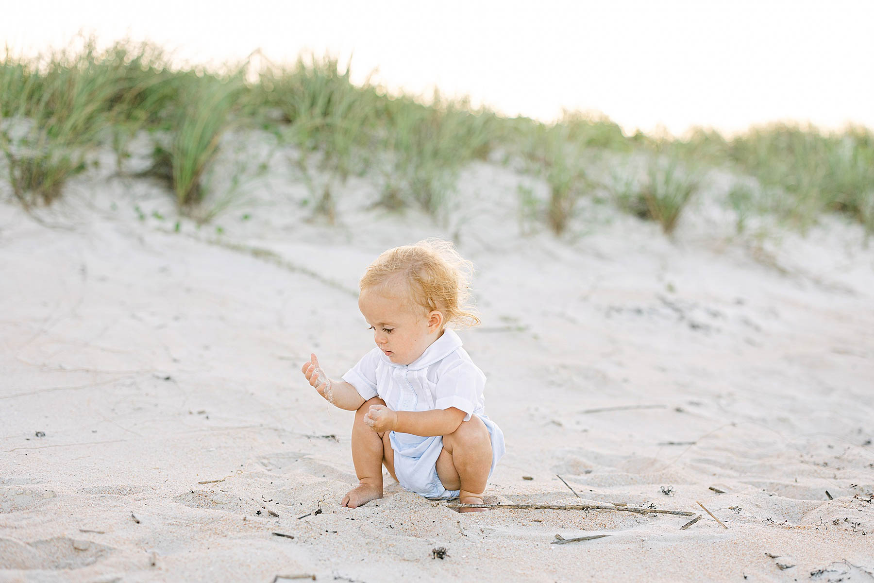 baby boy on playing with sand on the beach at sunset wearing white shirt