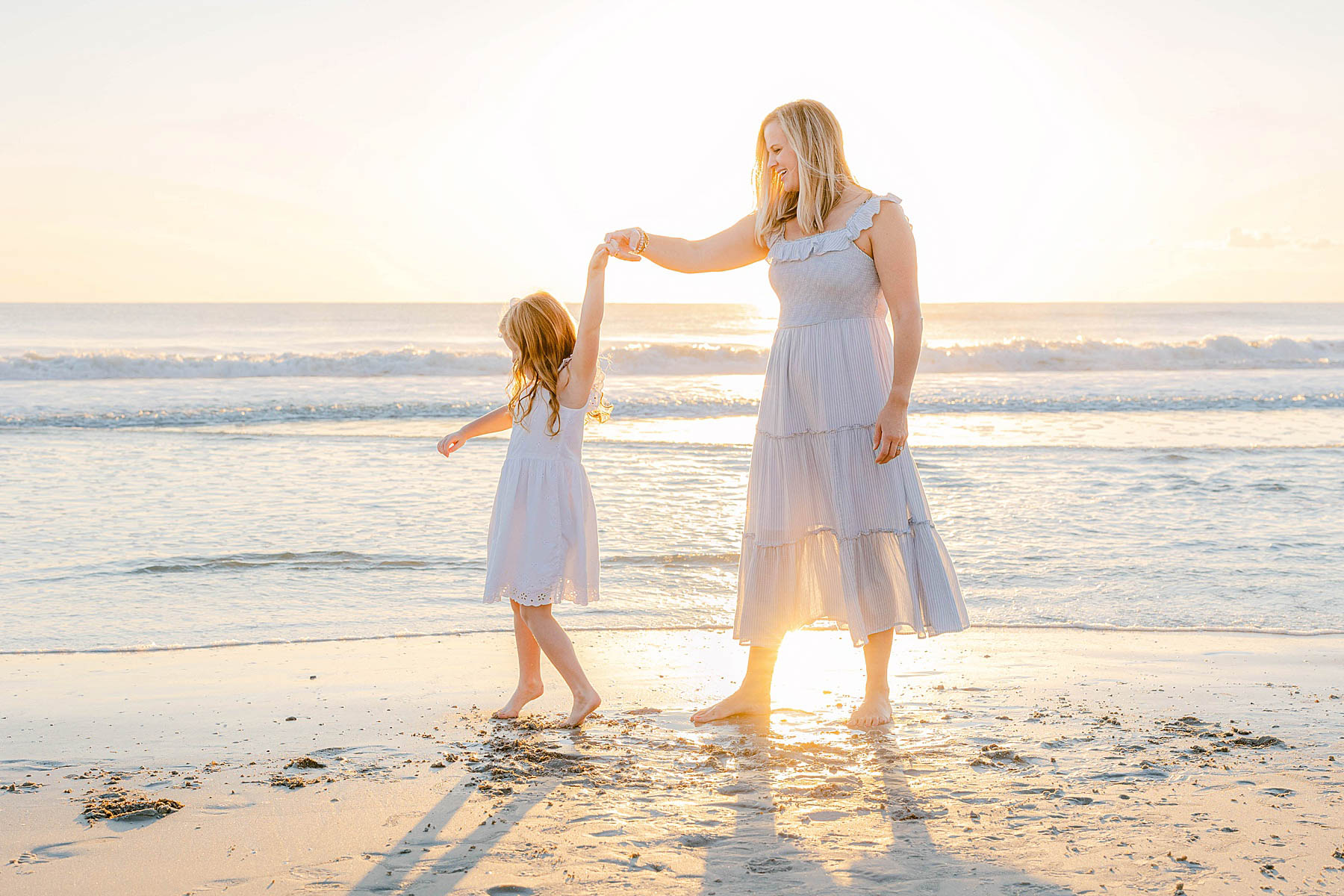 woman dancing with little girl on the beach at sunrise wearing pastel blue