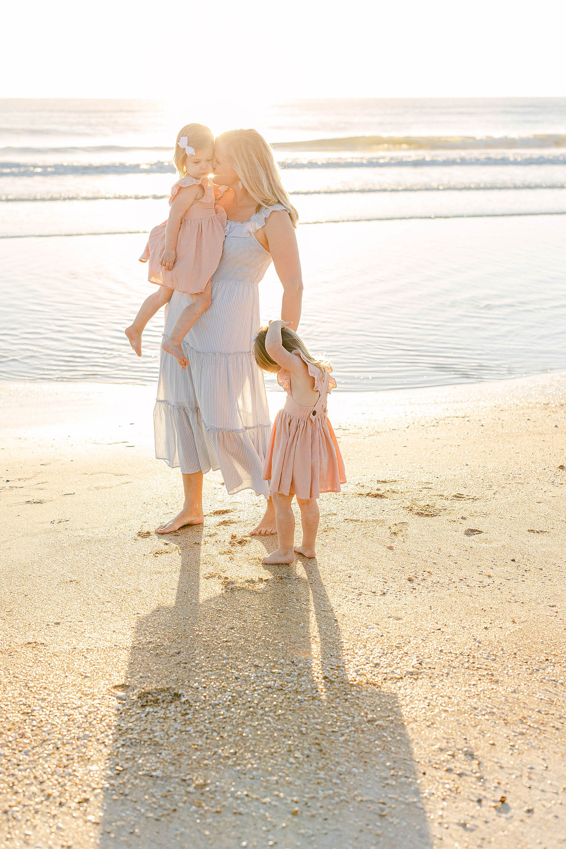 woman holding two little girls at sunrise on the beach