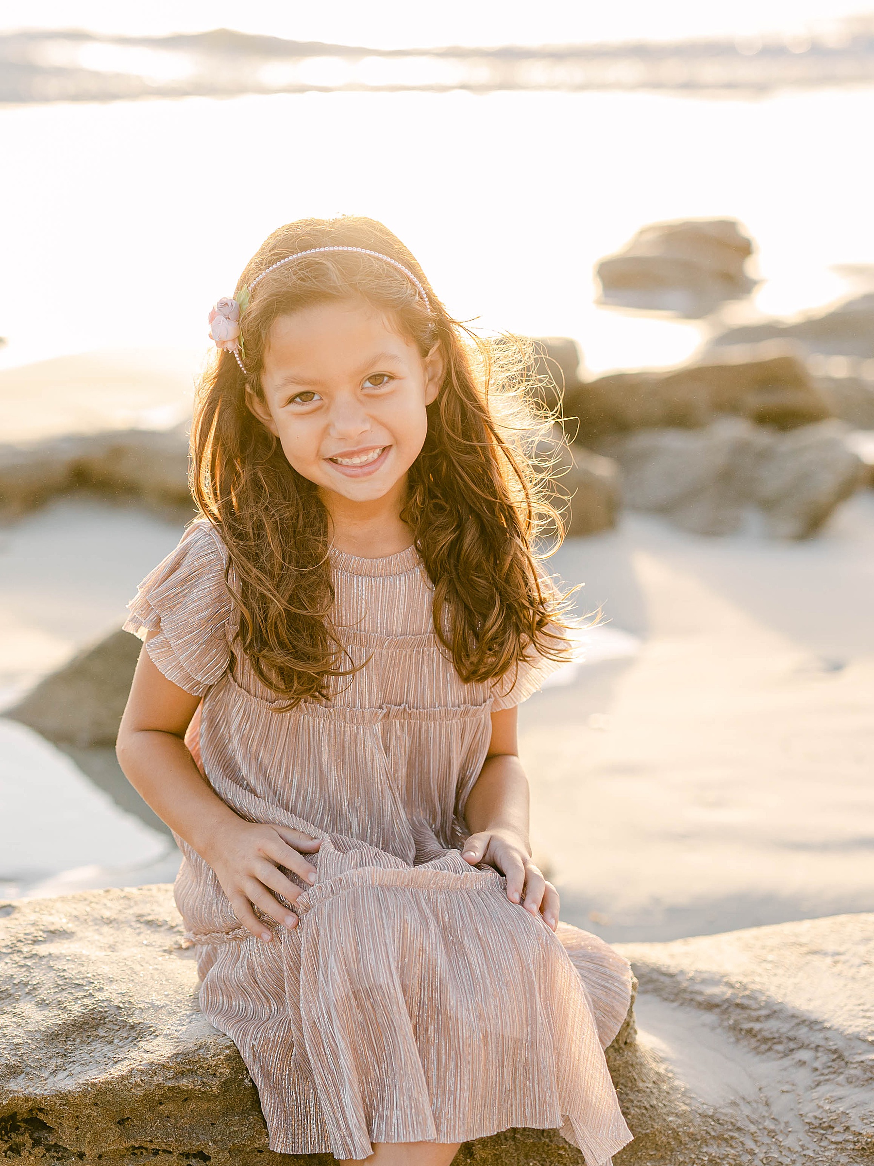 little girl at sunrise on the beach wearing metallic shimmer dress and smiling