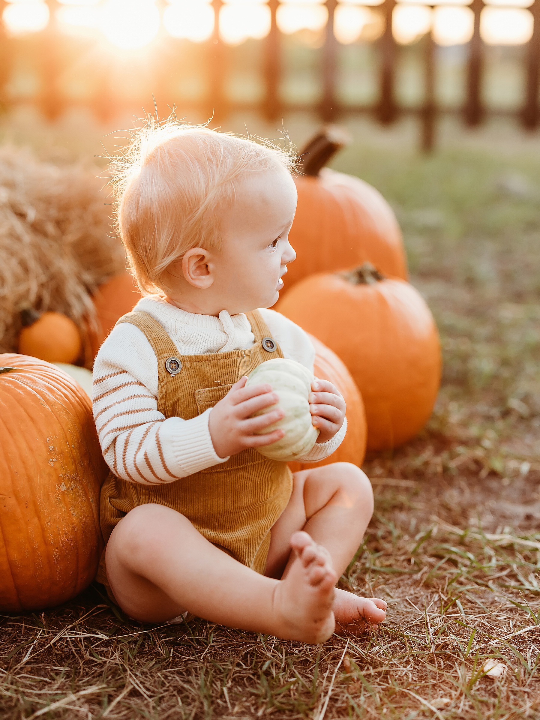 baby boy sitting in a pumpkin patch wearing corduroy overalls