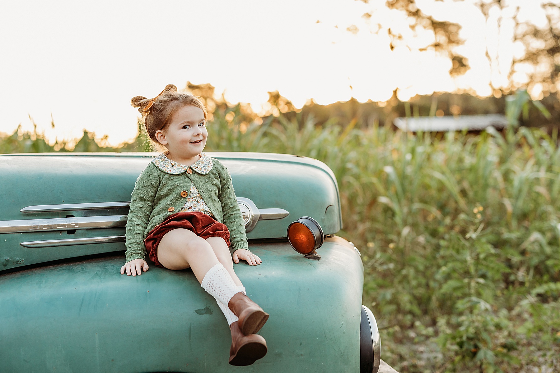 little girl sitting on a green truck in a green sweater on the farm