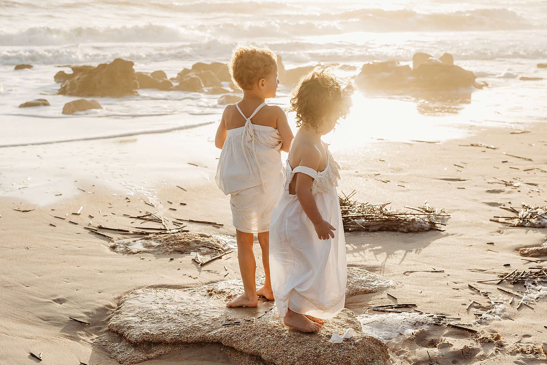 little girls in white dresses playing at the beach on the rocks at sunrise