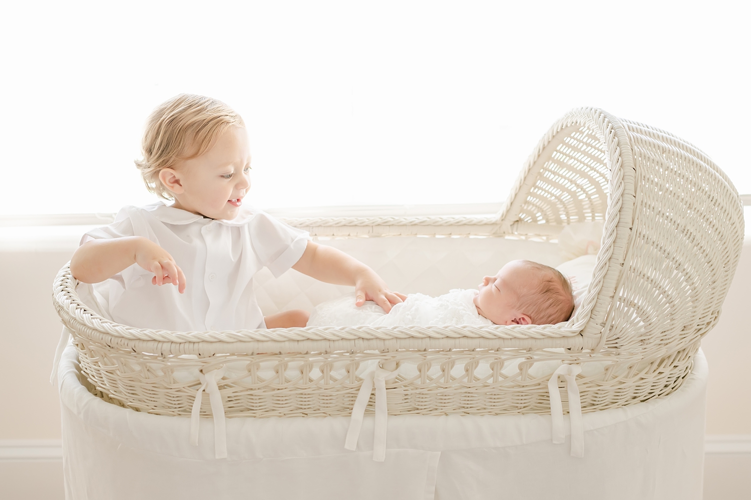 baby boy dressed in white sitting in bassinet in baby girl white nursery 