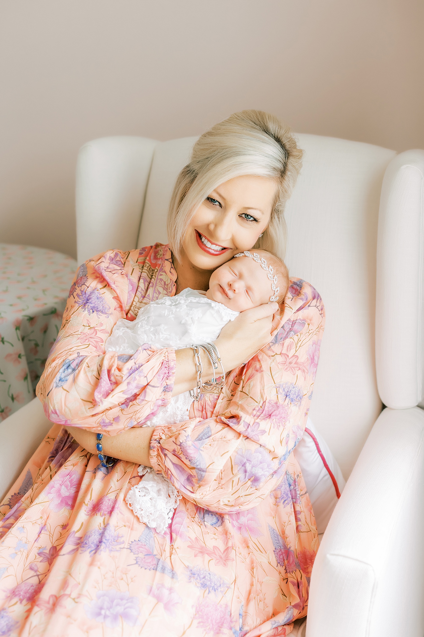 woman in pink maxi dress holding newborn baby girl in white chair