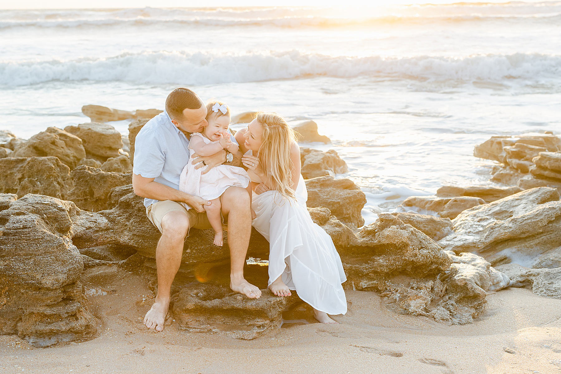 family with baby standing on the beach at sunrise wearing pastel colors