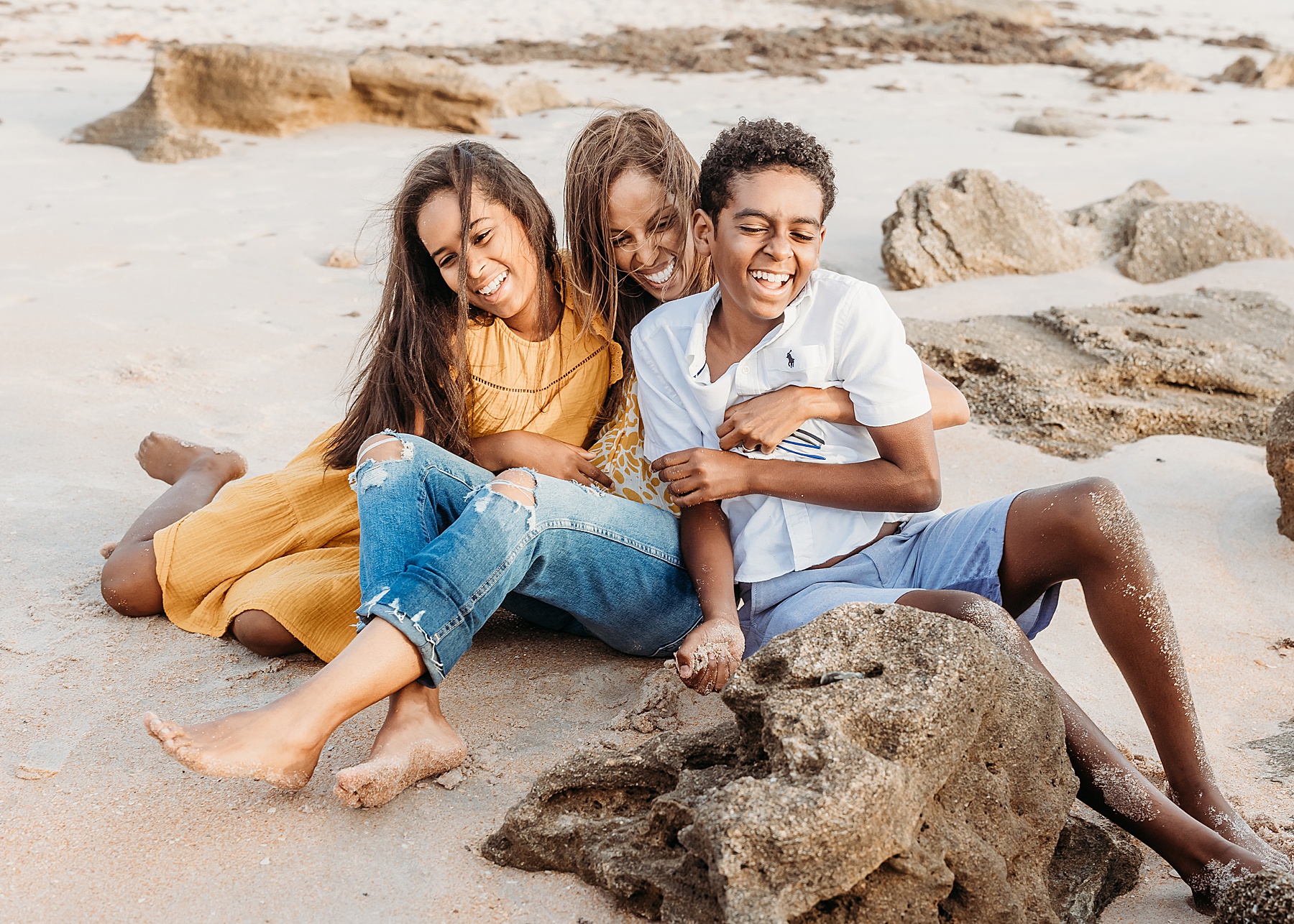 family pop three sitting on the sand at the beach laughing together