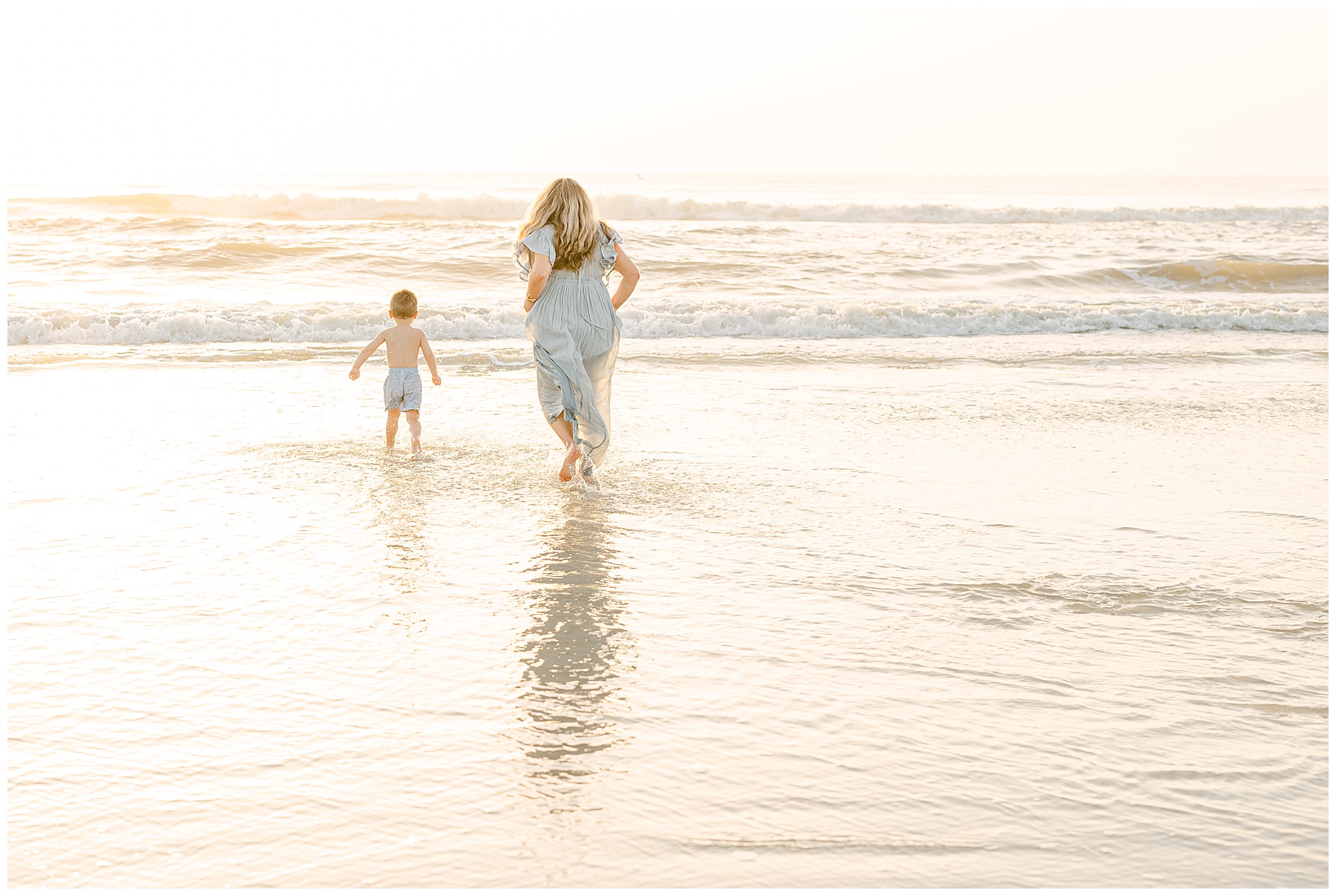 woman in sage green maxi dress chasing little boy into the water at sunrise in saint augustine beach florida